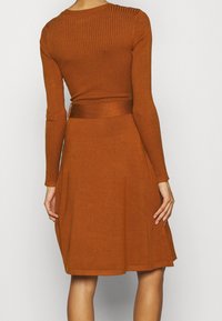 Ribbad, långärmad topp i rostfärg som matchas med en figurnära, utsvängd kjol, som visar en mjuk textur och en slät yta.