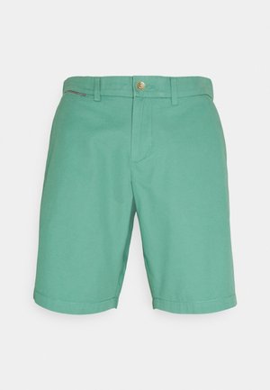 Grønne knælange shorts med bæltestropper, frontknap og lynlås lukning, samt en lille flagdetalje på højre side nær linningen.