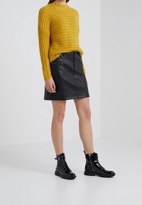 Żółty sweter z dzianiny, czarna skórzana mini spódniczka z zamek błyskawicznym oraz czarne lakierowane botki na sznurówki z bocznymi zamkami.