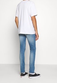 Camiseta blanca de algodón de manga corta, combinada con vaqueros ajustados de color azul claro y zapatillas negras, vista desde atrás.