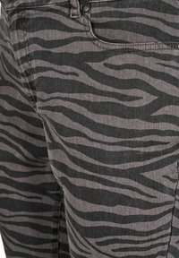 Jeans de mezclilla gris con un patrón de rayas de cebra negras, con un diseño clásico de cinco bolsillos y acentos de remaches metálicos.