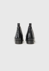 Bottines en cuir noir avec une finition brillante, dotées de panneaux latéraux élastiques, de languettes de tirage et d'un petit talon. Texture lisse avec un minimum de détails.