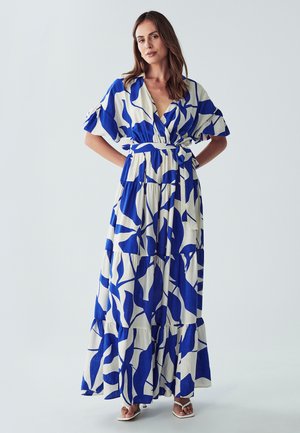 Maxi dress in blue and white with a leaf pattern, short puff sleeves, and a belted waist, made of lightweight fabric with a tiered design.