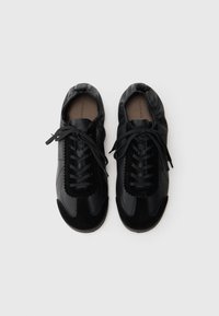 Schwarze Sneaker aus Leder und Wildleder mit runder Spitze, Schnürdesign und strukturierten Akzenten. Die Sohle ist beige.
