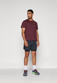 Mørkerød kortermet t-skjorte med hvit logo, kombinert med mørke shorts. Bruker fargerike treningssko med fremtredende lisser og demping.