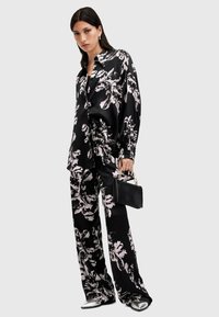 Conjunto de satén negro con estampado floral que incluye una camisa de corte holgado y pantalones de pierna ancha, combinado con calzado con detalles plateados y un pequeño bolso negro.