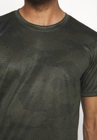 Zelené sportovní tričko s hexagonálním vzorem a černými akcenty. Krátké rukávy, kulatý výstřih, vyrobeno z prodyšné látky.