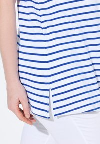 Modré a bílé pruhované tričko vyrobené z měkké tkaniny, má detail na straně a uvolněný střih, se šikmými pruhy po celé délce.