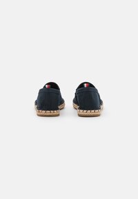 Paire d’espadrilles bleu marine à enfiler avec semelles en jute tissé, vues de dos sur fond blanc.