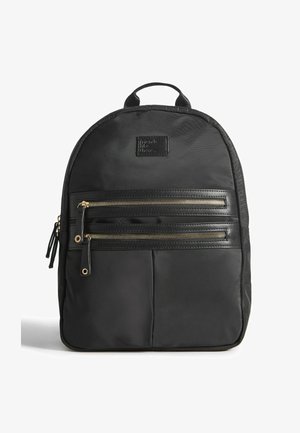 Must musta seljakott, millel on kaks kuldset tõmblukkudega taskut, tugevdatud käepide ja tekstureeritud pind. Omab ristkülikukujulist kuju, mille üle osa on ümar.