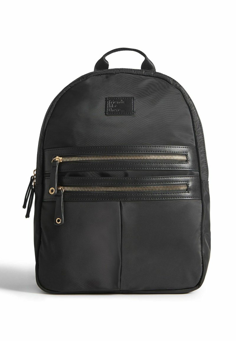 Sac à dos en nylon noir avec deux poches zippées dorées, une poignée renforcée et une finition texturée. Il présente une forme rectangulaire avec un haut arrondi.