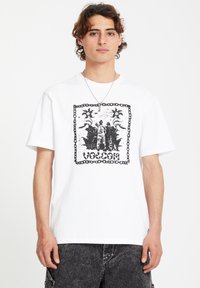White cotton t-shirt featuring a black graphic print with floral and figure motifs, framed by a chain-like border. Short sleeves, relaxed fit.
