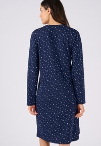 Vestito a maniche lunghe in cotone blu navy con stampa di mezze lune e pois bianchi, collo tondo, lunghezza al ginocchio e fessure laterali per facilitare i movimenti.