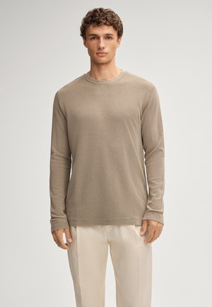 Beige Langarmhemd aus weichem Stoff mit Rundhalsausschnitt, geradem Schnitt und subtilen Nähten, kombiniert mit hellen Hosen.