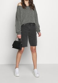 Harmaa olkaimeton neule, mustat farkkibermudashortsit revityllä helmalla, valkoiset lenkkarit ja pieni musta käsilaukku kahvalla.