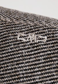 Détail de tissu tricoté en tons noir, blanc et beige. Présente un motif texturé avec un logo brodé subtil.