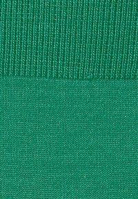 Tessuto verde brillante che mostra una trama liscia e lavorata a maglia, con costine visibili lungo la parte superiore, creando un aspetto uniforme.