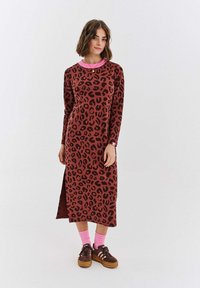 Dlouhé hnědé šaty s leopardím vzorem, dlouhými rukávy a růžovým límečkem. Mají boční rozparek a jsou doplněny růžovými ponožkami a hnědými botami.