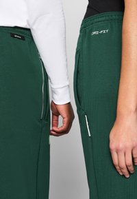 As calças de sweat verde Dri-FIT apresentam uma cinta elástica, bolsos laterais e etiquetas de marca. Um par tem um bolso com fecho éclair para maior comodidade.