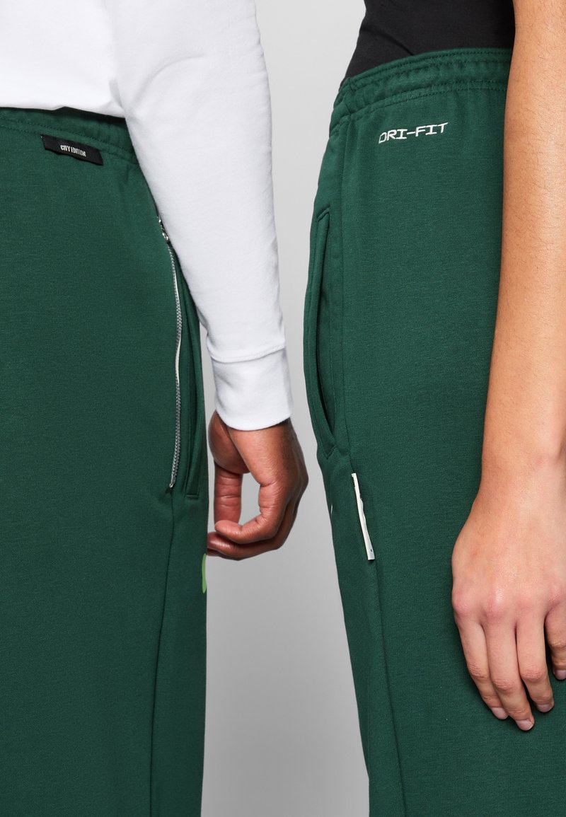 I pantaloni della tuta Dri-FIT verdi presentano una cintura elastica, tasche laterali e etichette di branding. Un paio ha una tasca con zip per maggiore comodità.