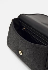 Borsa in pelle nera testurizzata con chiusura a pulsante dorato. L'interno include una tasca con cerniera e rivestimento nero liscio.