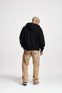 Zwarte hoodie met een losse pasvorm, gecombineerd met beige cargobroek met meerdere zakken. Schoenen zijn zwart met witte strepen.