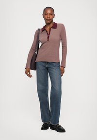 Ribbet langermet polo topp i mauve med burgunder krage og knapper, kombinert med lyseblå rettbente jeans og svarte sko. Tilbehør en veske.