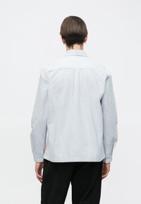 Ilgomis rankovėmis marškiniai su apykakle, šviesiai mėlynos ir baltos spalvų dryžuoti, su užsegamomis rankogaliais ir oranžine žyme šone.