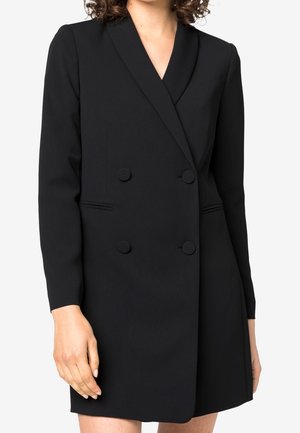 Vrouw draagt een zwart double-breasted blazerjurk met lange mouwen en een diepe V-hals.