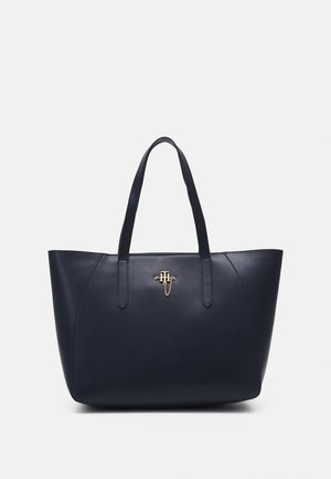 Marineblauwe leren tas met dubbele handvatten en een klein gouden monogramembleem in het midden vlak bij de bovenkant.