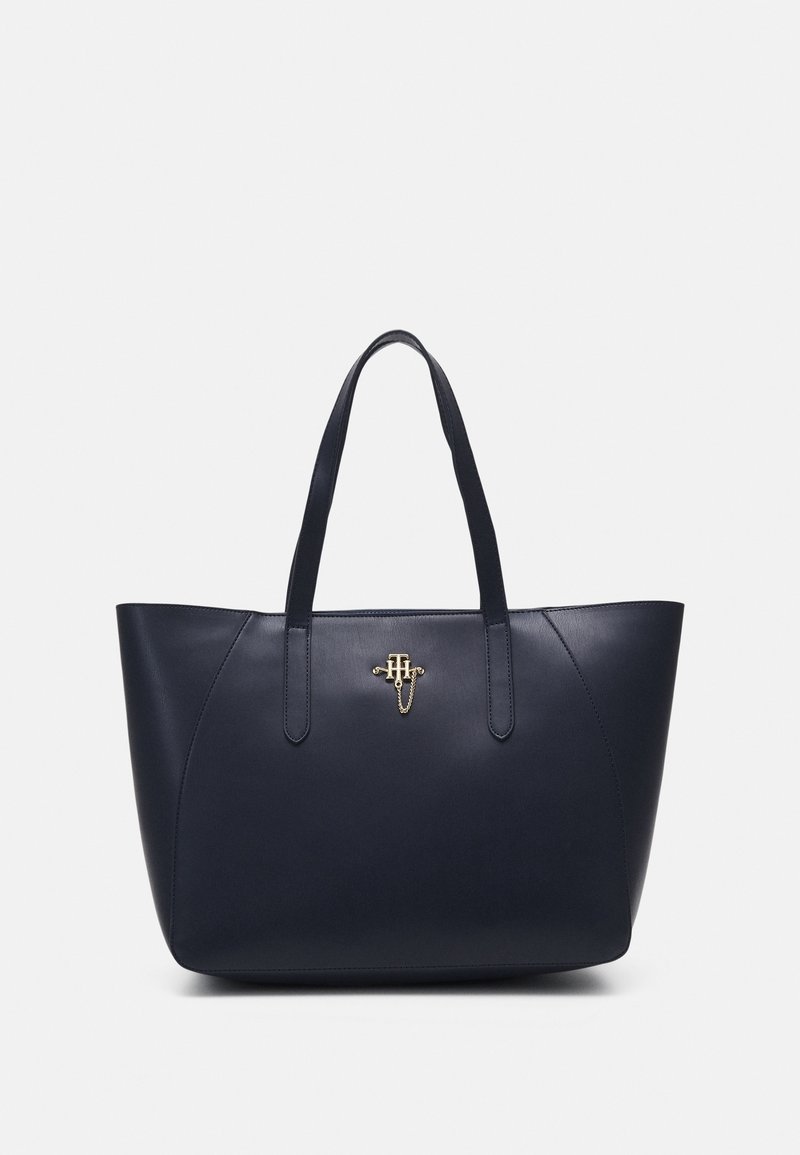 Sac cabas en cuir bleu marine avec double poignée et petit emblème monogramme doré centré près du haut.