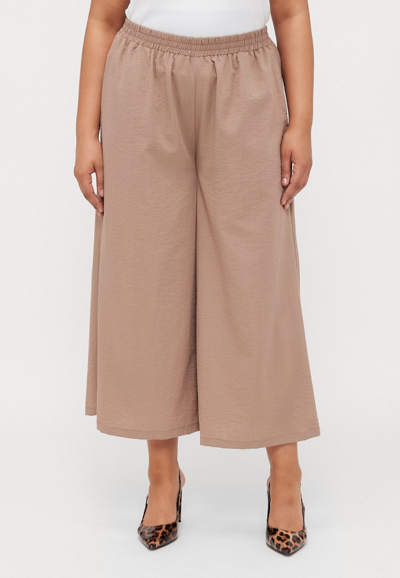 Light brown, wide-leg pants with an elastic waistband, made from a textured fabric. Paired with pointed leopard print heels.