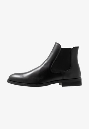 Bottine Chelsea en cuir noir avec panneau élastique latéral et petit talon empilé, présentée de profil sur fond blanc.