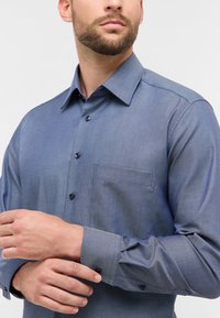 Camicia slim-fit a bottoni in un pattern a spina di pesce blu, dotata di una tasca sul petto, bottoni neri e un colletto strutturato.