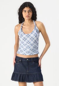 Top halter de cuadros azul claro con fruncidos, combinado con una falda de mezclilla oscura con dobladillo con volantes y bolsillos frontales.