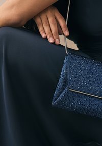 Navy blue clutch bag with textured surface, adorned with shiny blue beads, and a silver chain strap; elegant triangular design.