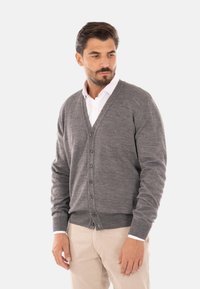 Cardigan grigio lavorato a maglia con scollo a V, cinque bottoni davanti, maniche lunghe e polsini a costine, abbinato a una camicia bianca sotto.