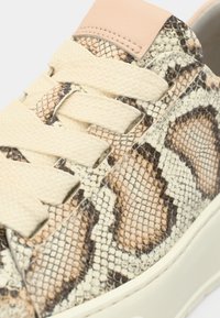 Αθλητικά παπούτσια με υφή φιδίσιας εκτύπωσης σε μπεζ και καφέ αποχρώσεις, με κρέμ κορδόνια και γλώσσα από δέρμα σε ανοιχτό ροζ χρώμα.