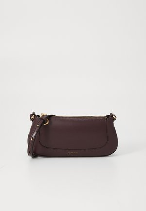 Bolsa de couro bordô da Calvin Klein com formato arredondado, fecho de zíper, alça ajustável e logotipo discretamente em relevo. Acessórios em dourado.