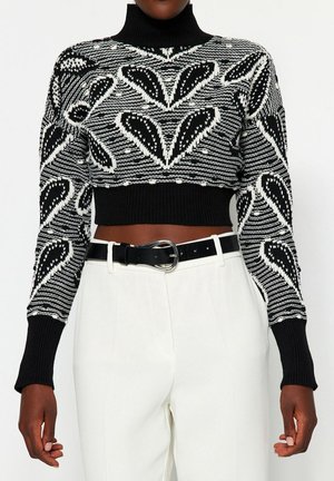 Czarnobiały krótki sweter z golfem w abstrakcyjne wzory liści, połączony z białymi, wysokim stanem spodniami i czarnym paskiem z srebrną klamrą.