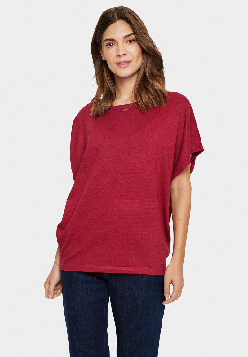 Haut rouge surdimensionné à manches courtes avec un col rond. Fabriqué en tissu doux et texturé, il présente une coupe décontractée et des fentes sur les côtés pour faciliter les mouvements.