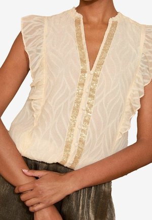Licht crèmekleurige blouse met ruches aan de korte mouwen, een decoratief gouden pailletten beleg en een textuur met golfpatroon. Knopenrij aan de voorkant.