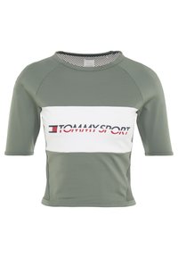 Camiseta deportiva de manga corta en verde olivo con un panel horizontal blanco que presenta el logo "TOMMY SPORT". Textura de malla a los lados.