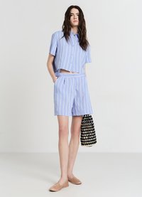 Hellblau-weißer gestreifter, kurzärmeliger Cropped-Shirt, kombiniert mit passenden Shorts und einer gewebten schwarzen und beigen Tasche.