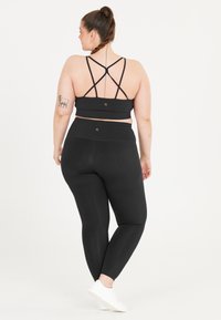 Zwarte sport-bh met kruislings gesneden banden en bijpassende high-waisted legging. Gladde stof met subtiele logo-accenten. Witte sneakers zichtbaar.