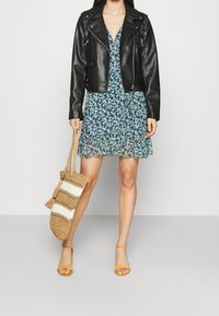 Černá kožená motorkářská bunda přes modrou květinovou šaty s vrstveným lemem. Žluté sandály na řemínky a tkaná slámová taška se pruhovaným vzorem.