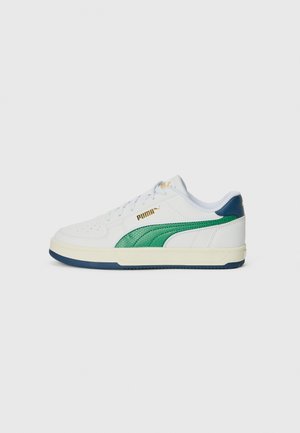 Witte sportieve sneaker met groene en donkerblauwe accenten, voorzien van een geperforeerde textuur, platte veters en een rubberen zool. Branding aan de zijkant.