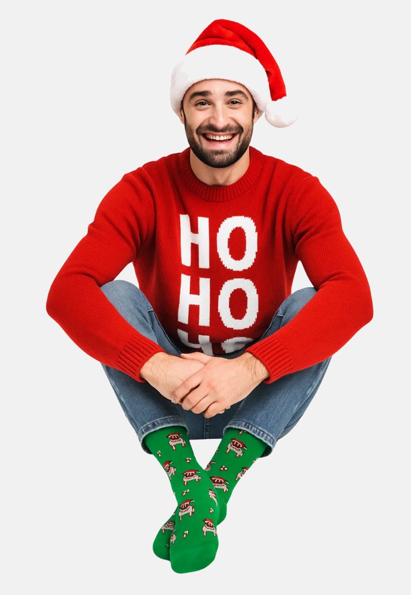 Red sweater with white "HO HO HO" text, blue jeans, and green socks featuring patterned holiday designs, paired with a white and red Santa hat.