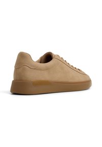 Sneaker in pelle scamosciata beige con profilo basso, punta arrotondata, chiusura con lacci frontale e suola in gomma testurizzata. Presenta cuciture e accenti minimali.