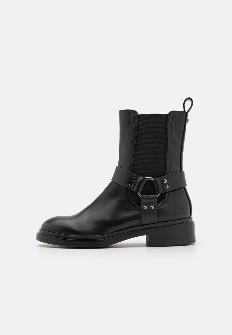 Black leather ankle boot featuring elastic side panels, a decorative band with a circular metal accent, and a low block heel.